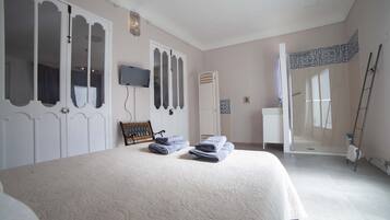 Een slaapkamer met een groot bed, een aan de muur bevestigde televisie en een badkamer zichtbaar door een geopende deur.