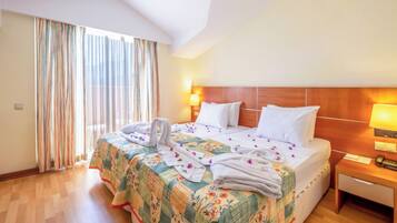 Habitación de hotel con una cama grande, cabecera de madera, mesita de noche y ventana con cortinas.