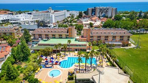 A resort with a large swimming pool, multiple buildings, and a view of the ocean.