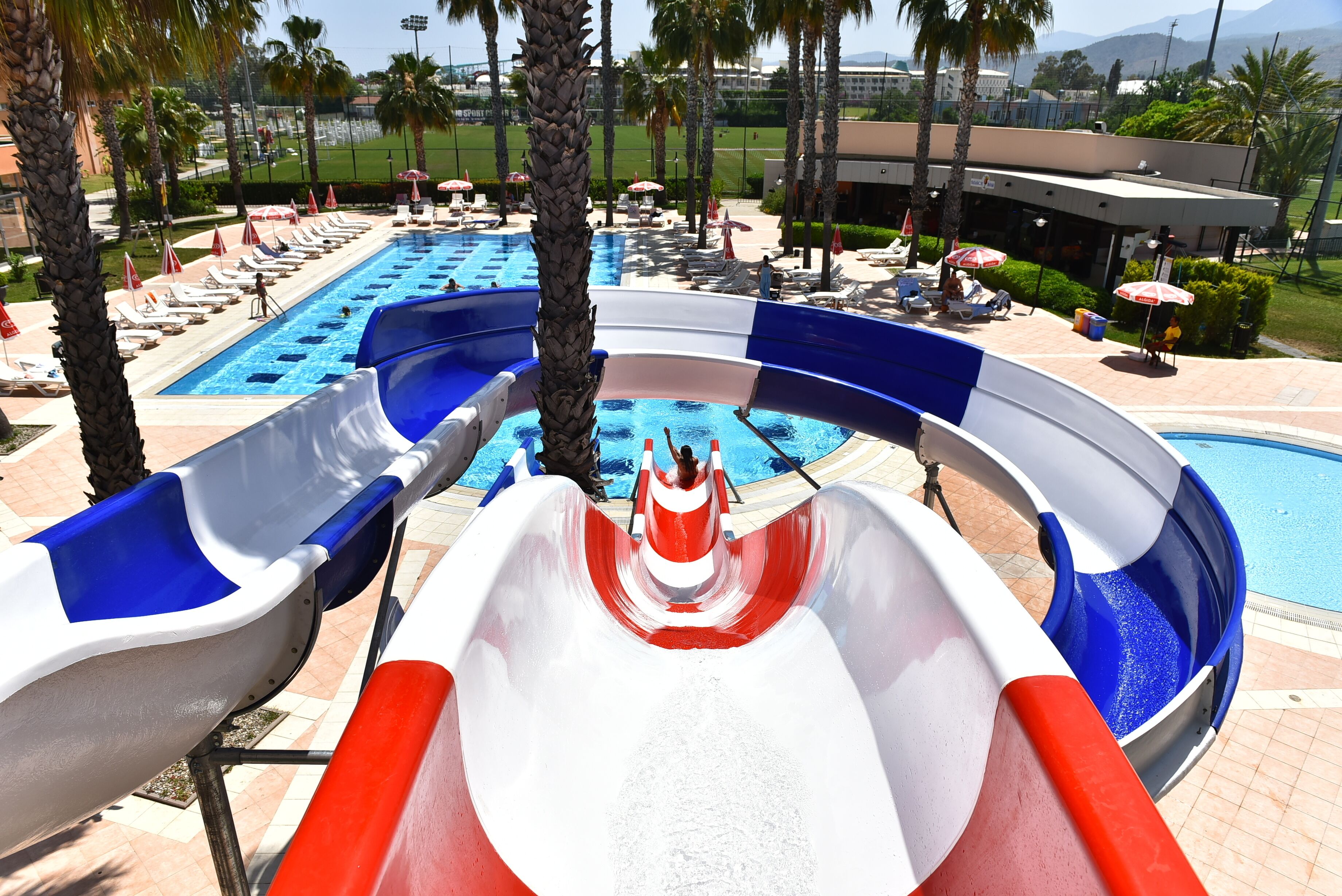 A water park with two slides, a pool, and lounge areas with umbrellas.
