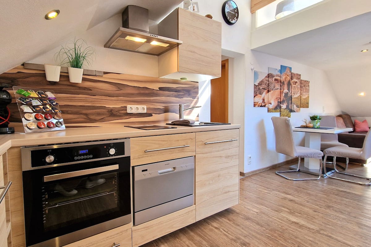 A modern kitchen with wooden cabinets, a built-in oven, and a coffee machine.