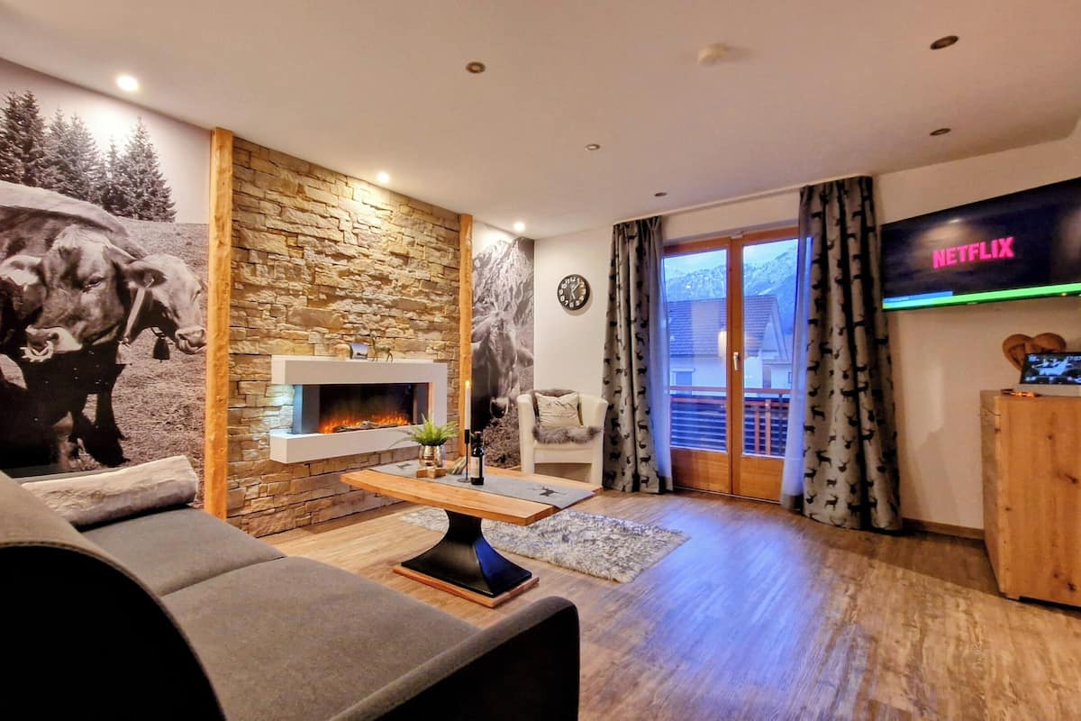 A living room with a stone wall, a fireplace, a sofa, a TV, and a view through a glass door.
