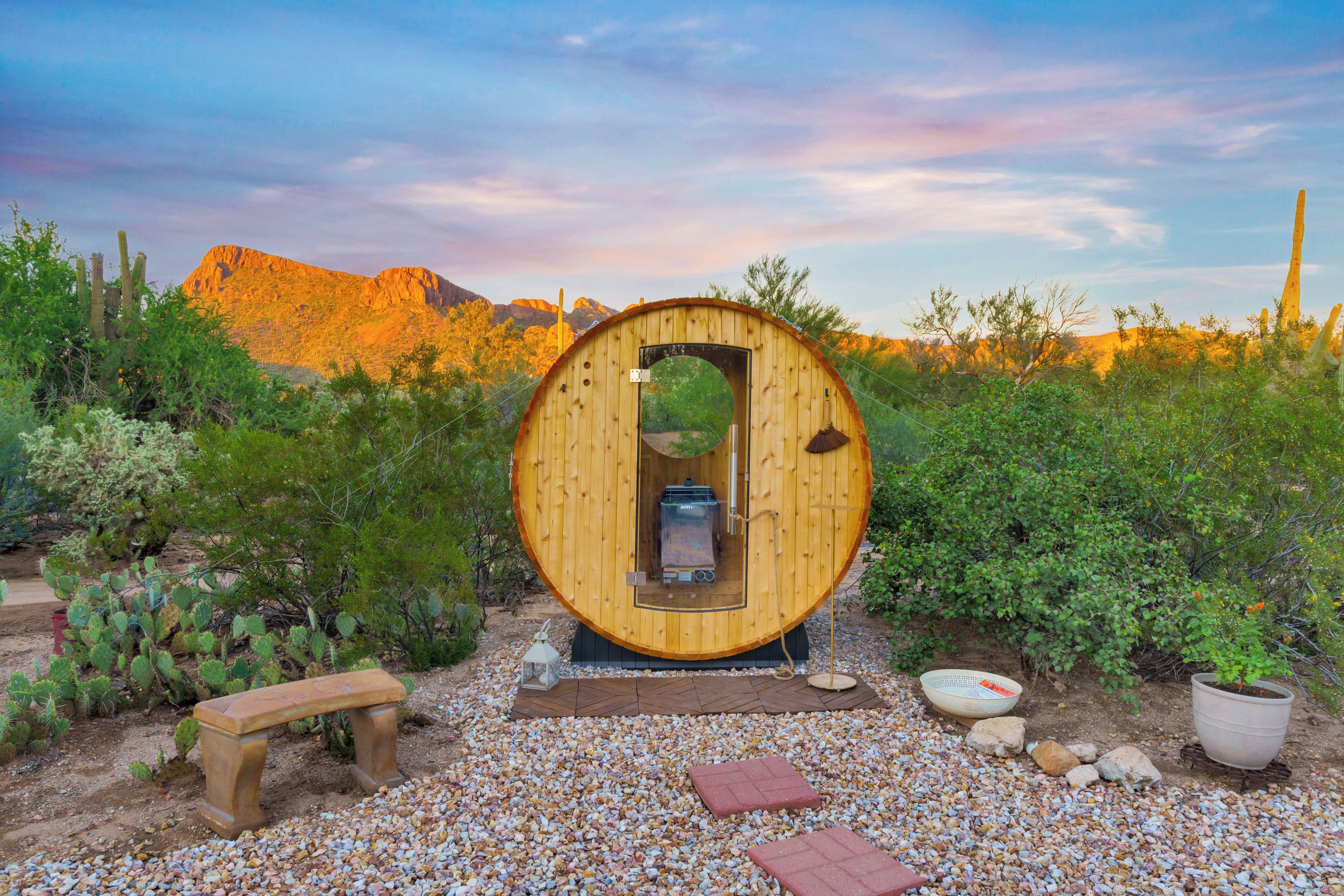 A wooden cylindrical structure with a door, surrounded by desert vegetation and a mountain in the background.