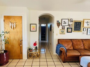 A living room with a brown leather sofa, a glass coffee table, a potted plant, and a wooden door with a dreamcatcher. - Bohemian desert sanctuary with stunning sauna/cold plunge retreat! (Tucson)