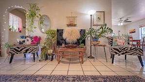Ein Wohnzimmer mit einem zentralen Rattanschreibtisch, Ohrensesseln mit ZEBRA-Muster und verschiedenen Topfpflanzen.
