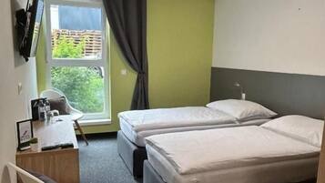 Ett hotellrum med två sängar, ett skrivbord, en stol, ett fönster med gardiner och utsikt över grönområden utanför.