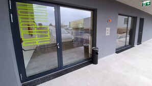 A building entrance with a glass door, a metal kick plate, and a small trash bin. - MOTEL Bad Vöslau (Bad Voeslau)