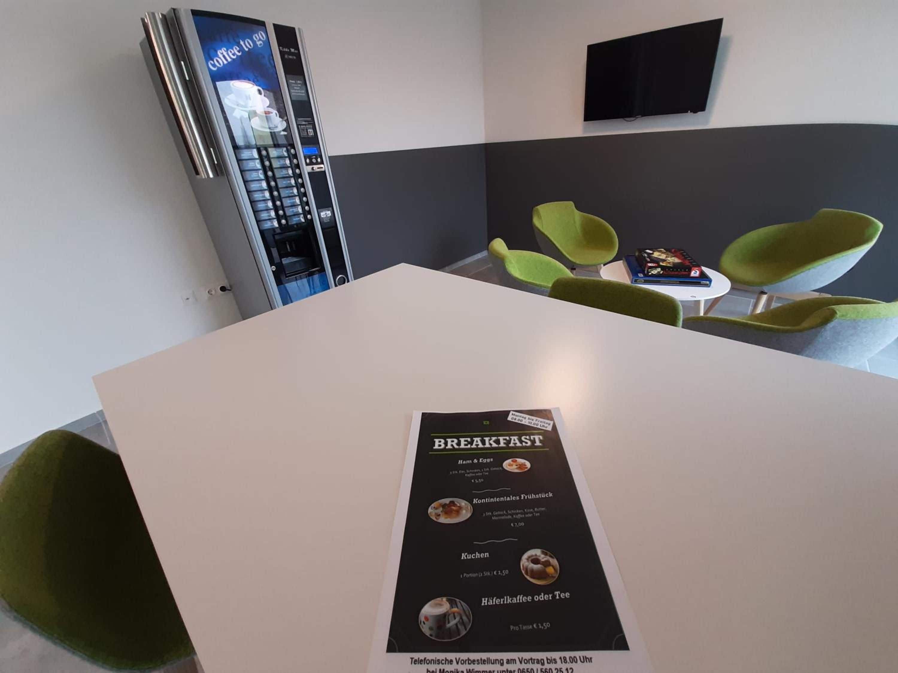 Un menú de desayuno sobre una mesa en una habitación moderna con sillas verdes y una máquina de café.