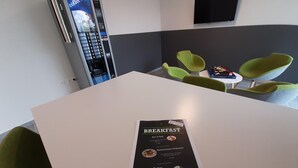 Un menú de desayuno sobre una mesa en una habitación moderna con sillas verdes y una máquina de café.