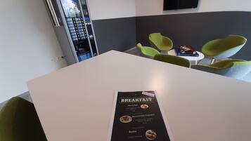 Un menú de desayuno sobre una mesa en una habitación moderna con sillas verdes y una máquina de café.