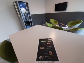 A breakfast menu on a table in a modern room with green chairs and a coffee machine. - MOTEL Bad Vöslau (Bad Voeslau)