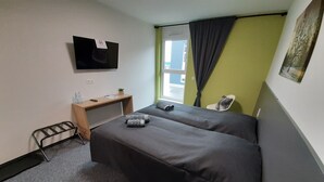 A hotel room with two beds, a desk, a chair, a TV, and a window with curtains. - MOTEL Bad Vöslau (Bad Voeslau)