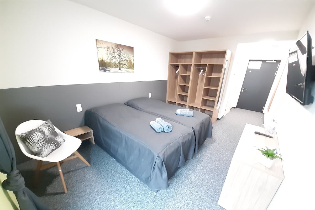 A bedroom with two beds, a chair, a desk, a wardrobe, and a television.