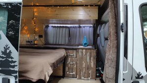 A compact RV interior with a kitchenette, a bed, and a small bathroom. - Self-built campervan (Kutaisi)