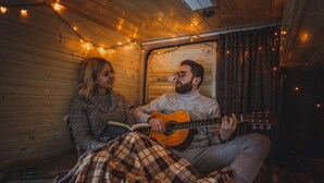 A cozy room with wooden walls, a bed with a plaid blanket, and a person playing a guitar. - Self-built campervan (Kutaisi)
