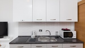 A modern kitchen with white cabinets, a black countertop, a sink, a kettle, a microwave, and a television.