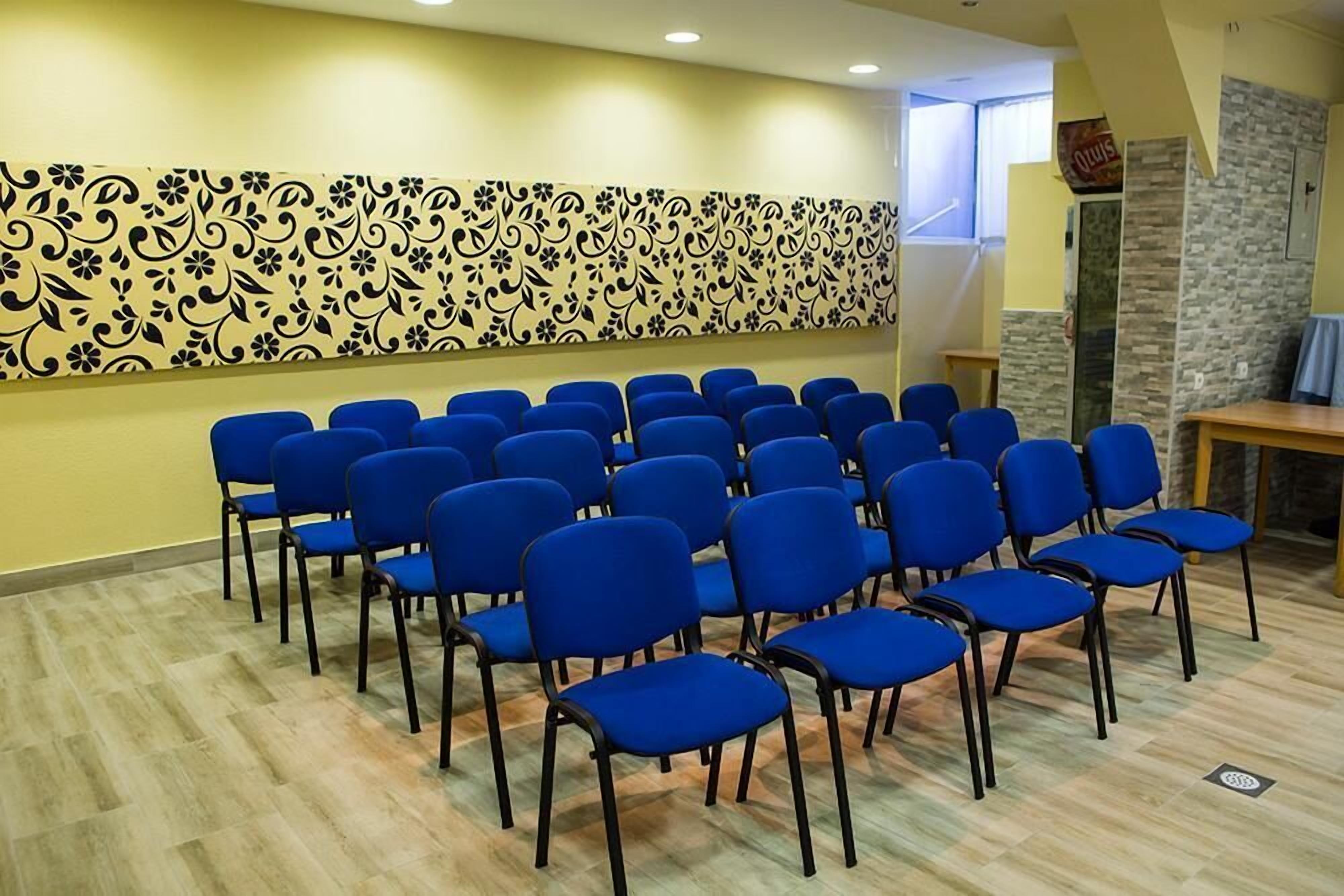 A conference room with rows of blue chairs, a patterned wall, and a stone wall with a window.