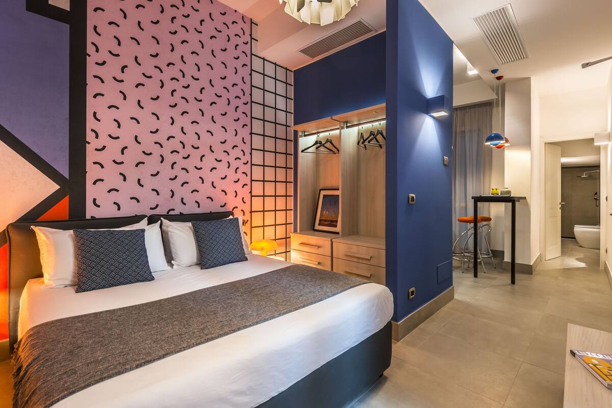 Ein modernes Hotelzimmer mit einem großen Bett, einem begehbaren Kleiderschrank und einem Badezimmer mit Dusche und Toilette.