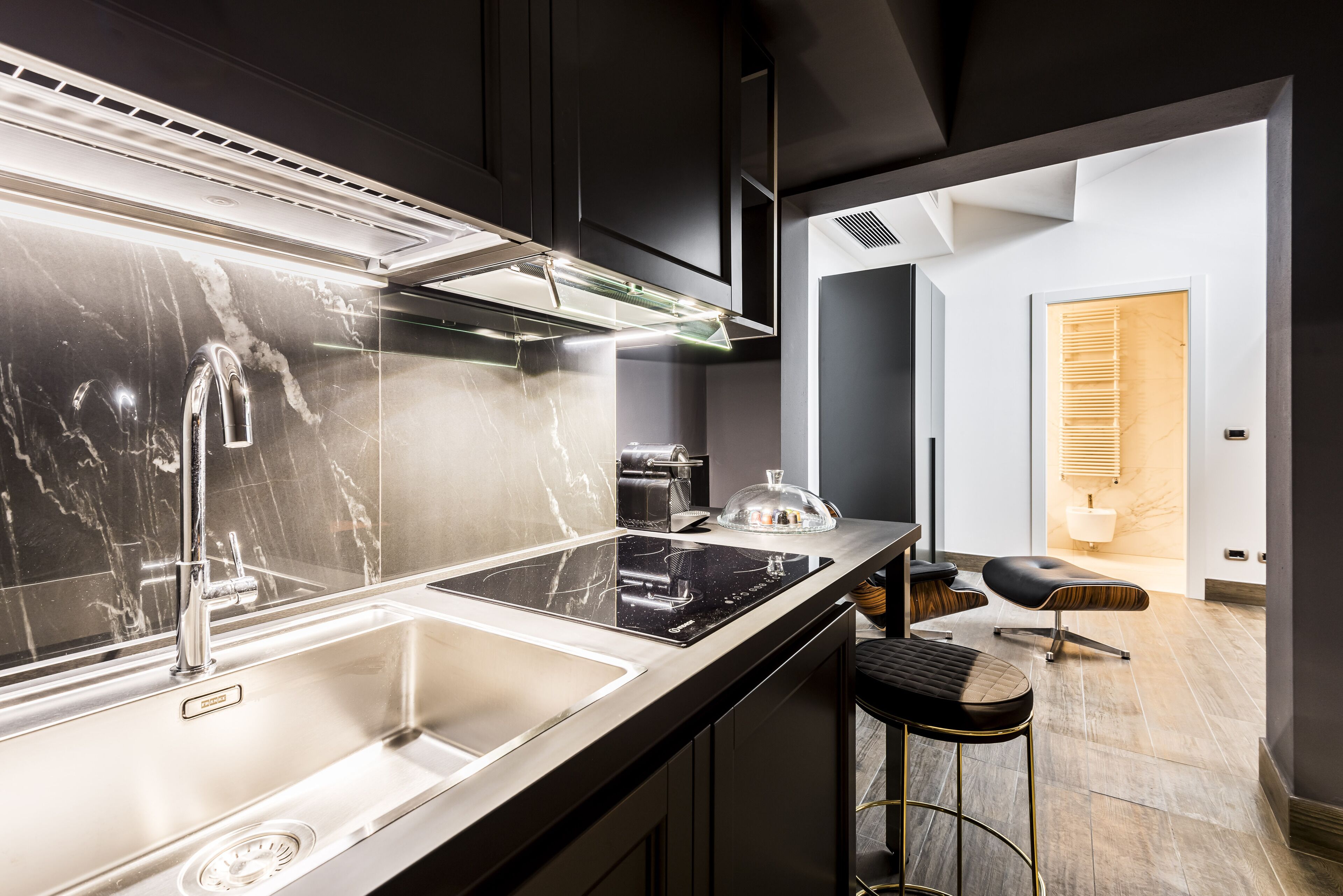 Een moderne keuken met een RVS-spoelbak, een zwart aanrecht en een glazen afdekking boven het fornuis.