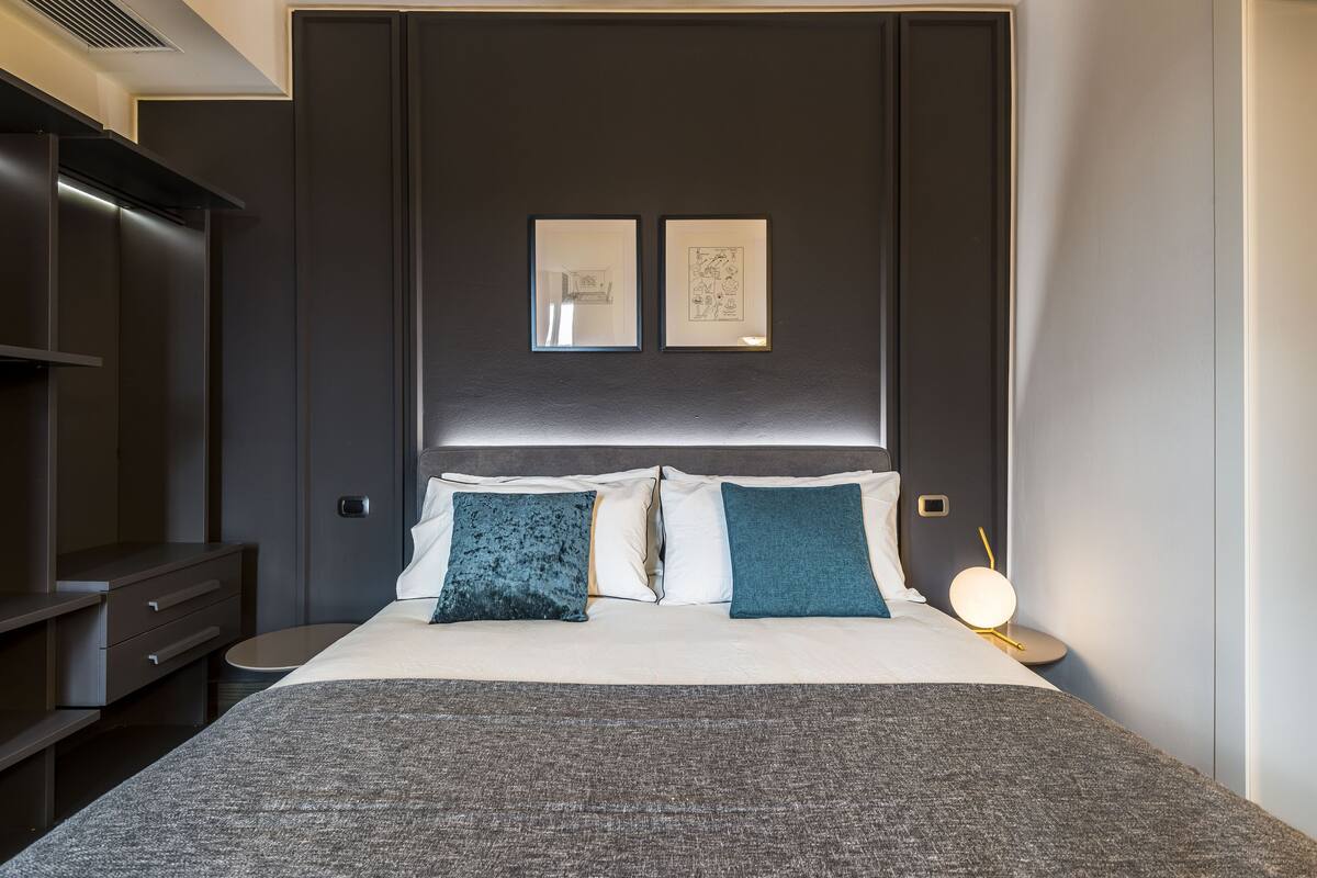 Ein modernes Hotelzimmer mit einem großen Bett, einem dunklen Kopfteil und zwei gerahmten Kunstwerken darüber.