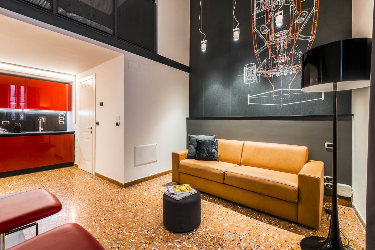 Ein stilvoller Wohnbereich mit einer Couch, einem Hocker und einer Küche im Hintergrund.