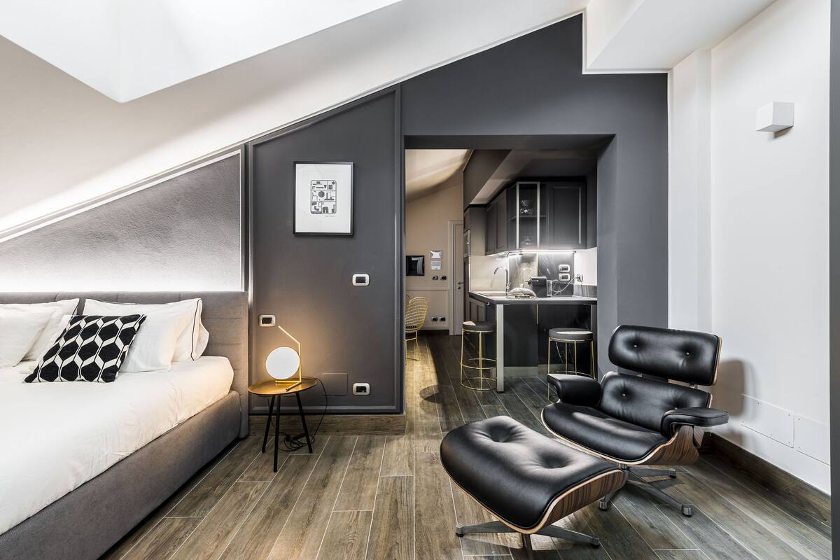 Ein modernes Hotelzimmer mit Bett, einer Sitzecke mit Sessel, einem Schreibtisch und einer Küchenzeile.