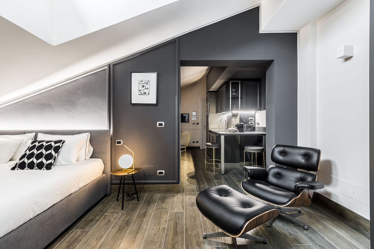 Ett modernt hotellrum med en säng, en sittgrupp med en stol, ett skrivbord och ett litet kök.