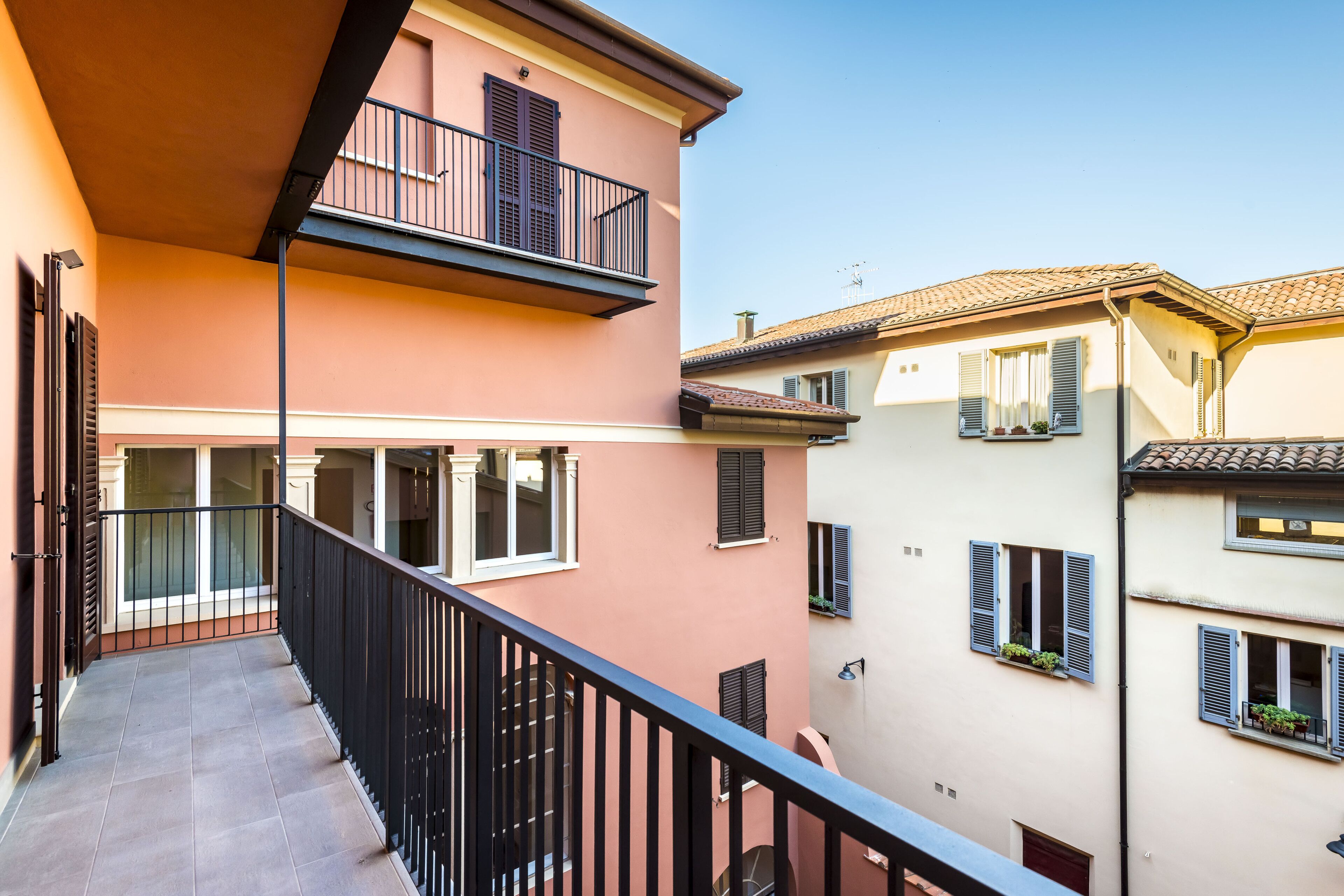 Un edificio de varios pisos con balcones, piso de baldosas y ventanas con contraventanas.