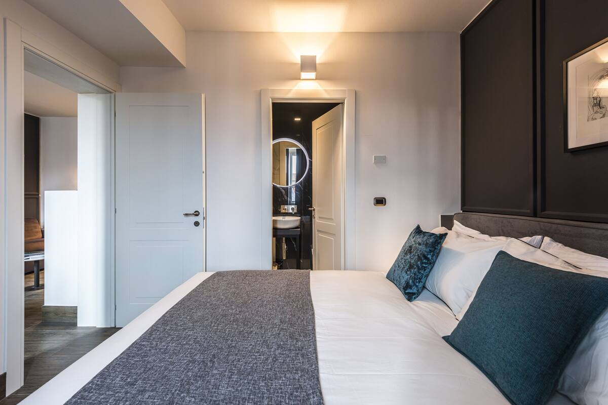Ein modernes Schlafzimmer mit einem großen Bett, einem Nachttisch, einem Spiegel und einer Tür zu einem Badezimmer.