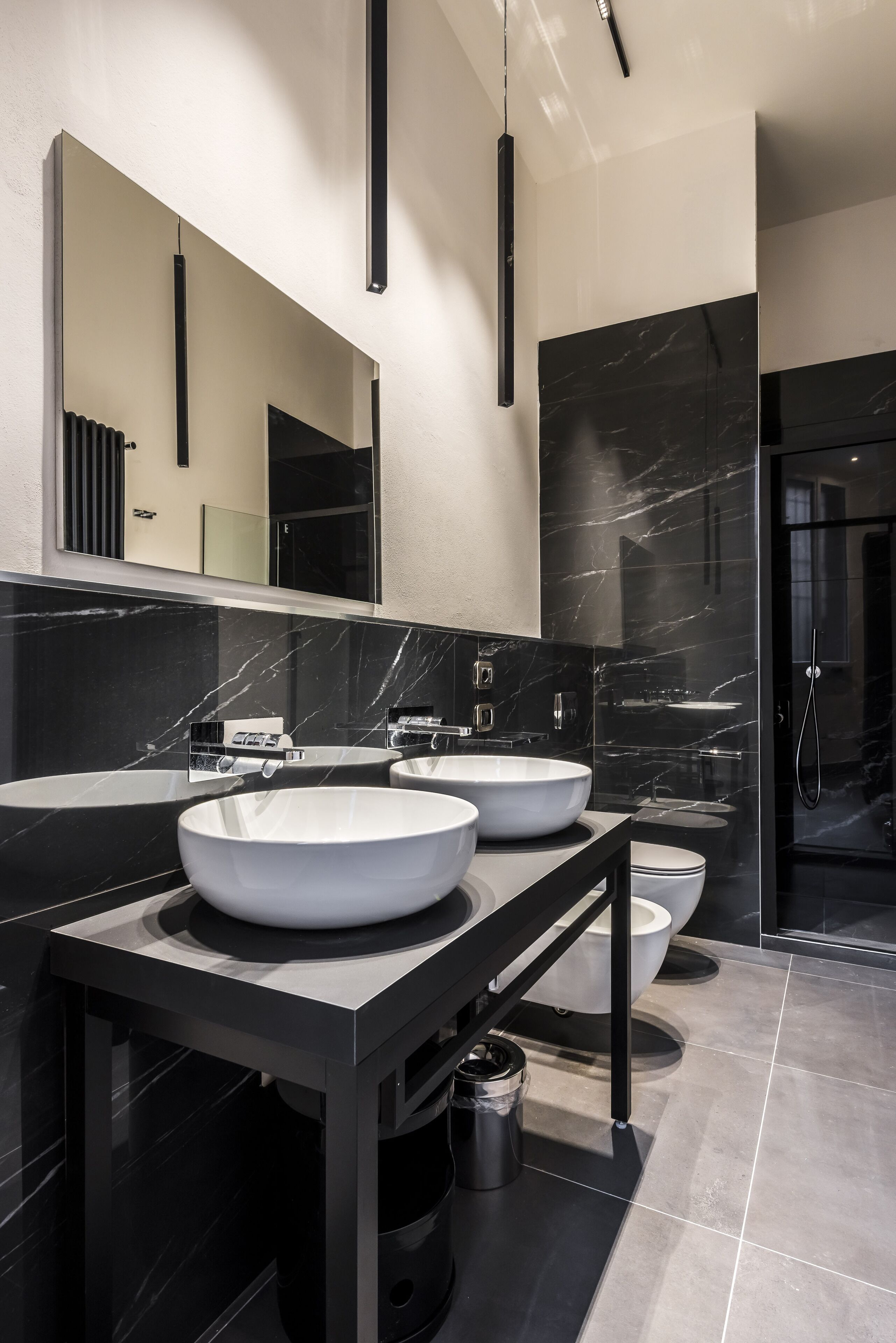 A modern bathroom with two large white sinks, a black vanity, and a glass-enclosed shower.