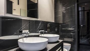 A modern bathroom with two large white sinks, a black vanity, and a glass-enclosed shower.