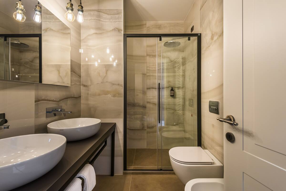 Ein modernes Badezimmer mit zwei großen weißen Waschbecken, einer gläsernen Duschkabine und einer Toilette.
