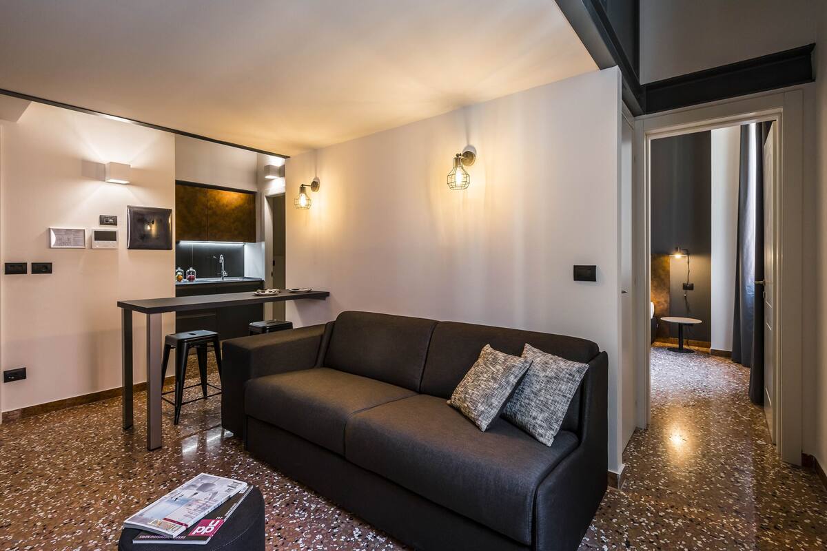 Ein modernes Wohnzimmer mit einer Couch, einem Couchtisch und einer Küchenzeile im Hintergrund.