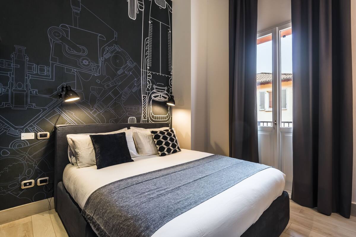 Ein modernes Hotelzimmer mit einem großen Bett, einem Kopfende mit schwarz-weißem Muster und einer Wand mit einem Bauplan-Design.