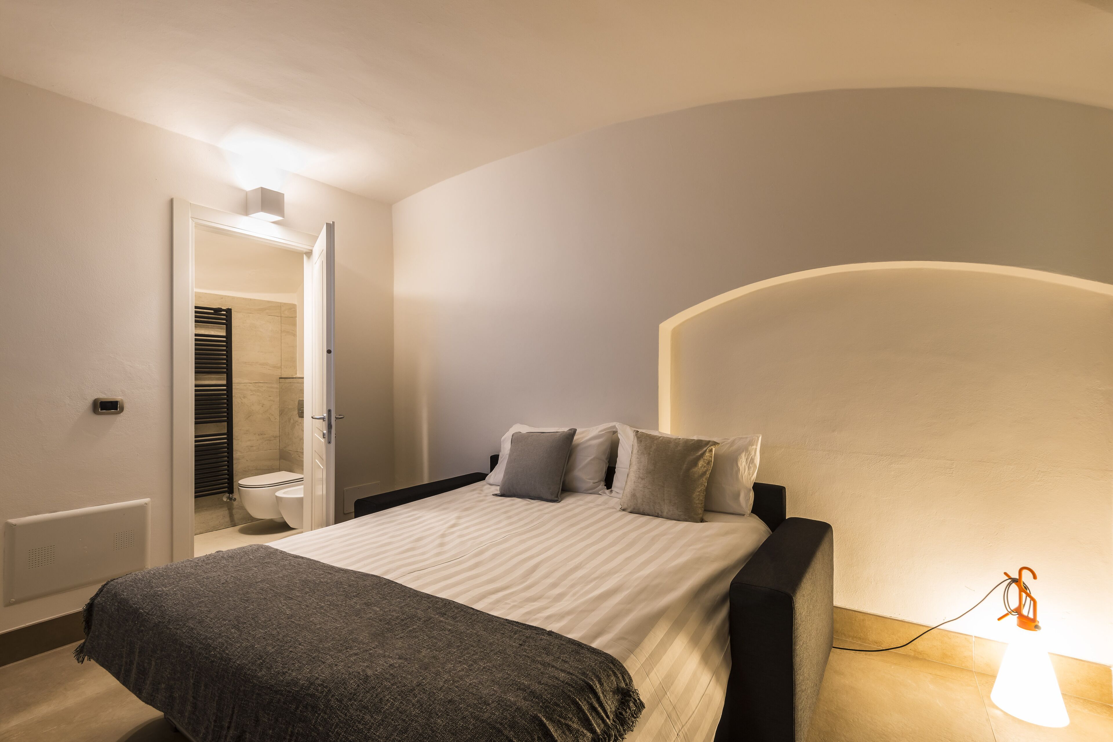 A bedroom with a bed, bedside table, and a wall-mounted lamp.