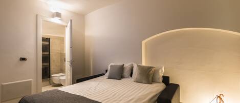 A bedroom with a bed, bedside table, and a wall-mounted lamp.