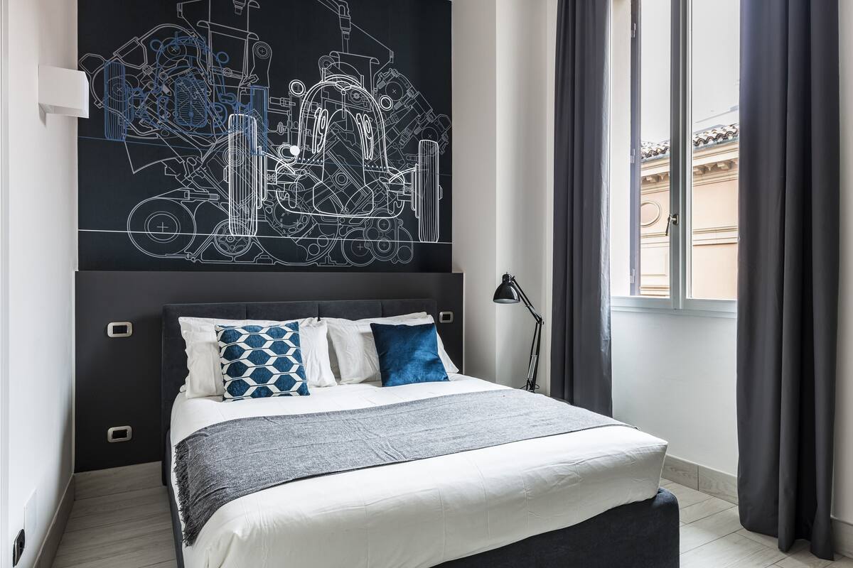 Ein modernes Schlafzimmer mit einem großen Bett, einem Kopfteil mit geometrischem Muster, einem Wandbild, einer Nachttischlampe und einem Fenster mit Vorhängen.