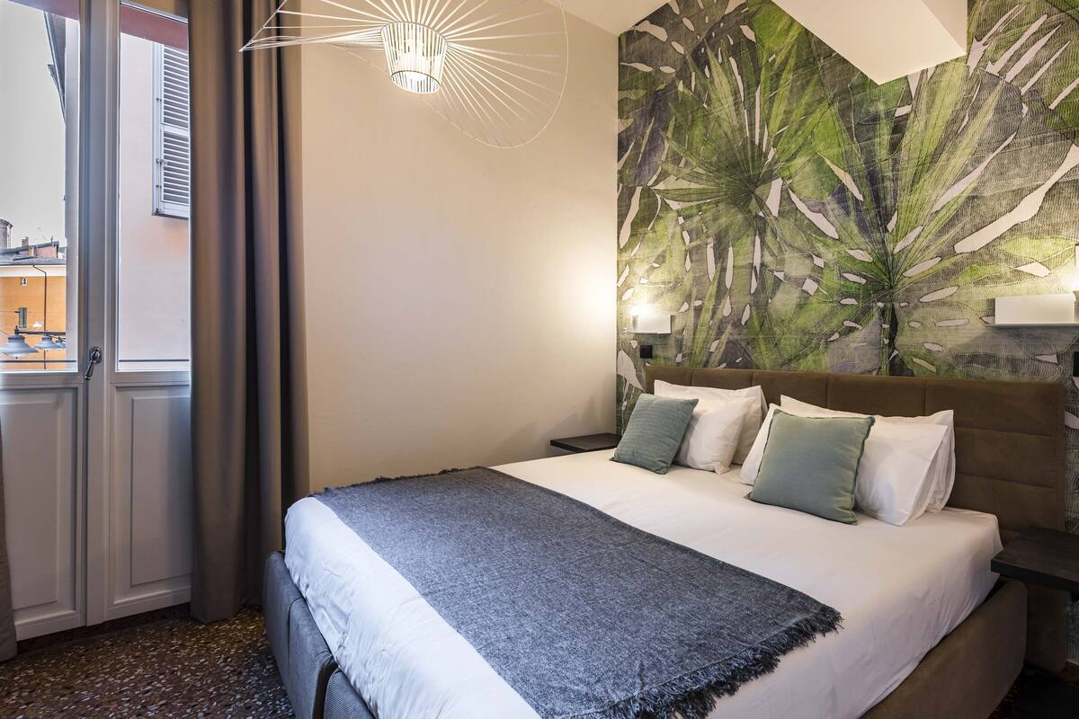 Ein Hotelzimmer mit Bett, einer großen Wandmalerei, einer Deckenleuchte und Blick durch eine Tür.