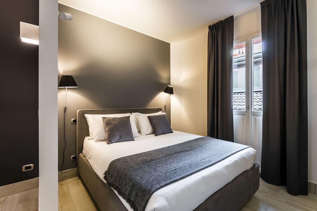 Ein modernes Schlafzimmer mit einem großen Bett, zwei Nachttischlampen und einem Fenster mit Vorhängen.