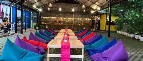 Un espacio al aire libre con sillones de mimbre coloridos y una mesa larga con un camino de mesa rosa.