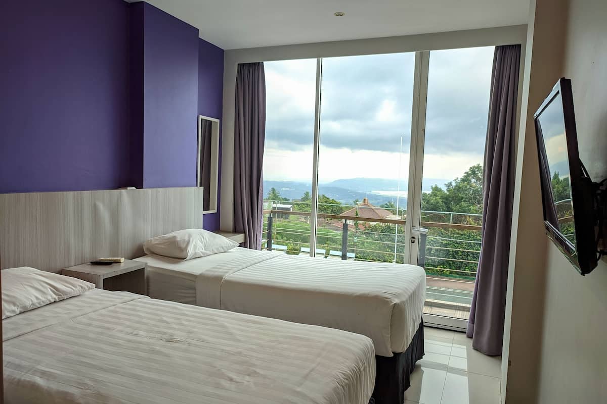 Habitación de hotel con dos camas, un ventanal con cortinas, un televisor de pantalla plana montado en la pared y vistas al exterior.