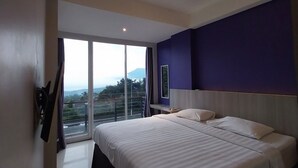 A hotel room with a large bed, a window with a view, and a ceiling light. - Terra Cassa Hotel (Bandungan)