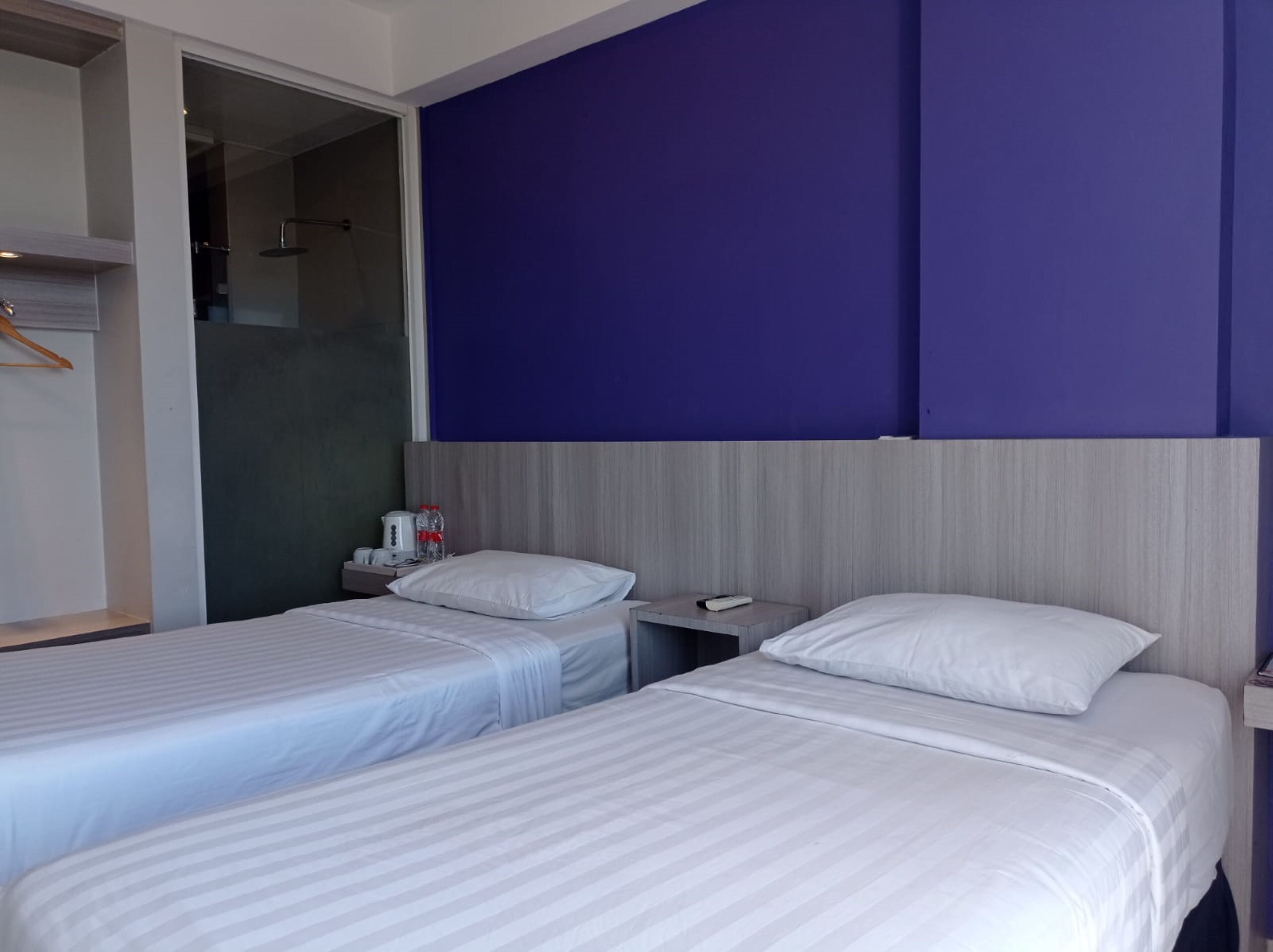 A hotel room with two beds, a wooden headboard, a nightstand, and a bathroom with a glass shower.