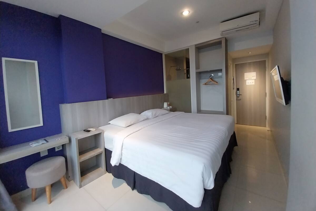 Habitación de hotel moderna con cama, mesita de noche y un taburete pequeño.