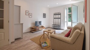 A living room with a sofa, a TV, a bookshelf, and a window with a view of greenery. - Gorgeous home in Rosignano Marittimo with house a panoramic view (Rosignano Marittimo)
