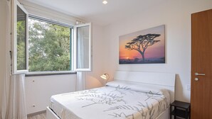 A bedroom with a bed, a bedside table, a nightstand, a window with curtains, a wall-mounted lamp, and a painting of a tree. - Gorgeous home in Rosignano Marittimo with house a panoramic view (Rosignano Marittimo)