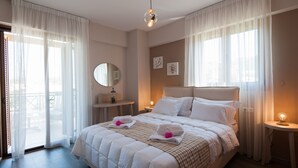 Una cama bien hecha con sábanas blancas y una manta a cuadros, una mesita de noche con lámpara, y un ventanal con cortinas de encaje.