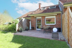 Una casa residencial con fachada de ladrillo, techo de tejas y un patio con mobiliario exterior.