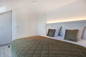 A modern hotel room with a large bed, a headboard with built-in lighting, and a door with a handle. - Vacationer village 43c, Germany (Ostseebad Boltenhagen)