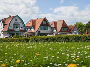 A row of traditional European-style buildings with sloped roofs, a central sign indicating a restaurant and café, and a well-maintained garden in the foreground. - Vacationer village 43c, Germany (Ostseebad Boltenhagen)